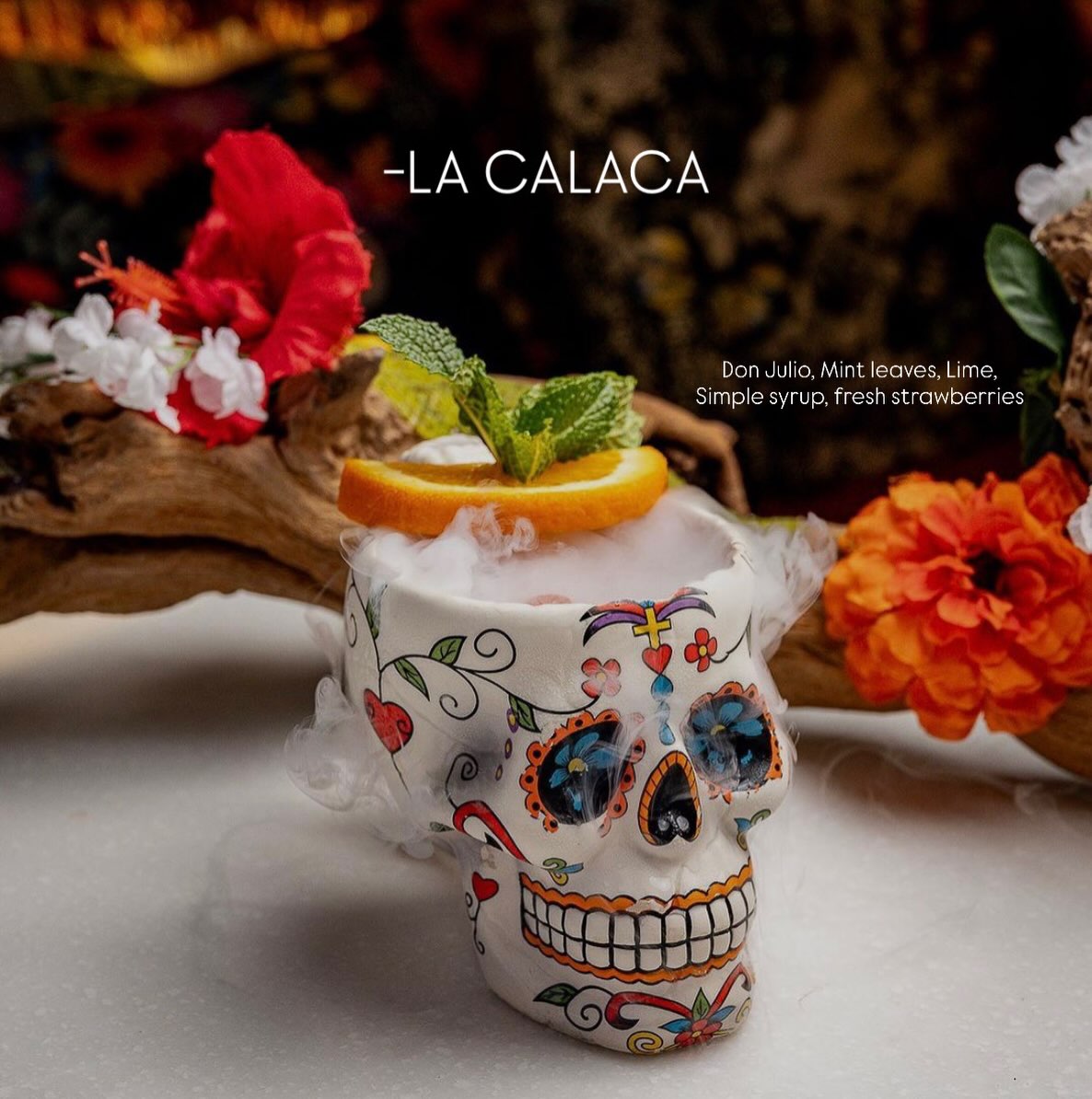 La Calaca cocktail close-up — sugar skull mug, marigolds, mint